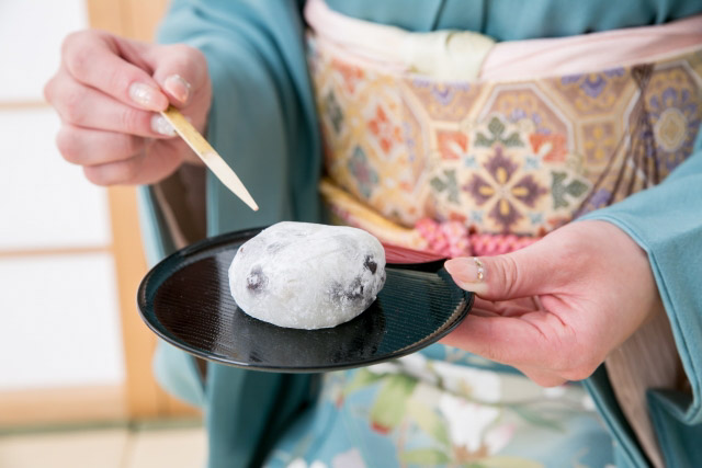 A woman wearing kimono and holding a daifuku on a small tray