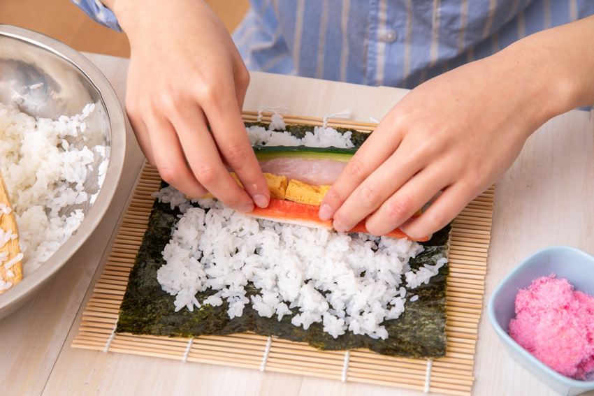 A person rolling a sushi roll with the help of a bamboo sushi roll mat