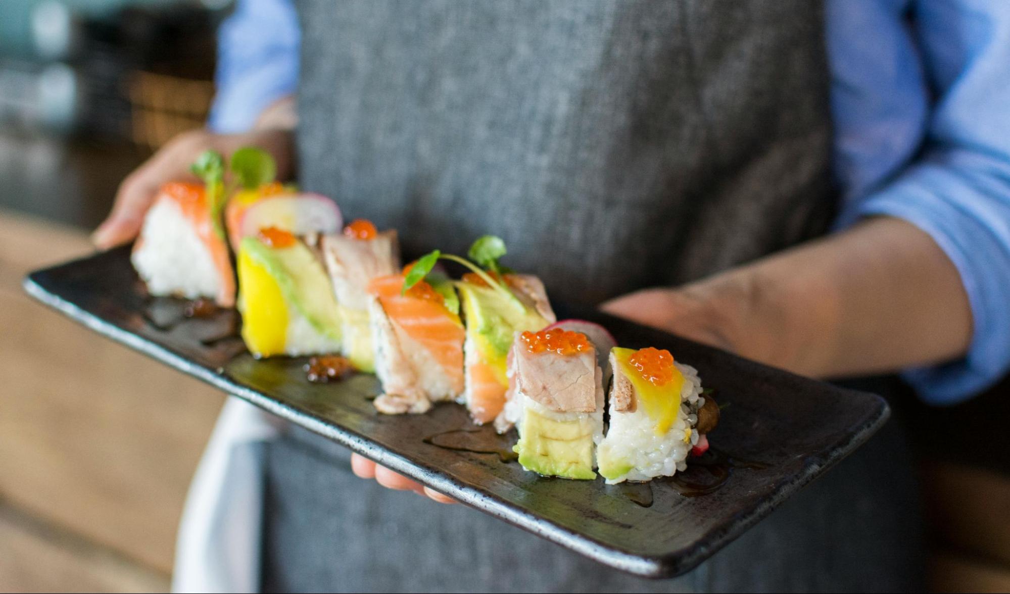 A person holding a plate with different types of sushi on it