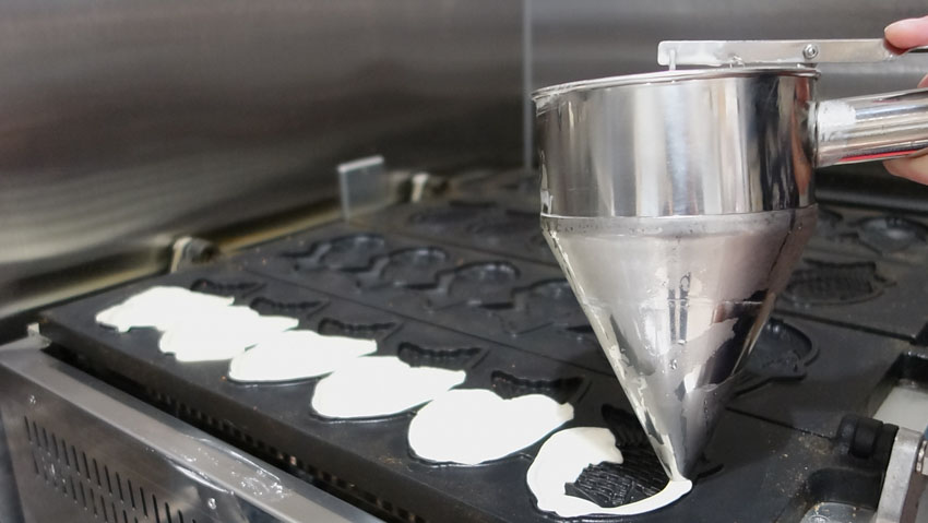 Taiyaki batter being poured onto a large taiyaki iron