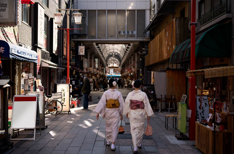 Two women dressed in kimono walking down a Japanese city street