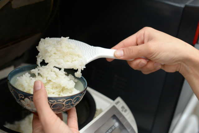 Close up of a pair of hands filling a rice bowl with cooked rice from a rice cooker