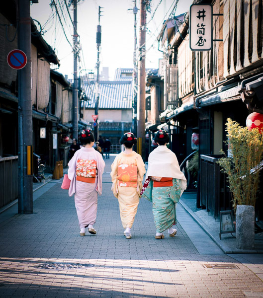 Three Geisha walking down an old style Japanese street