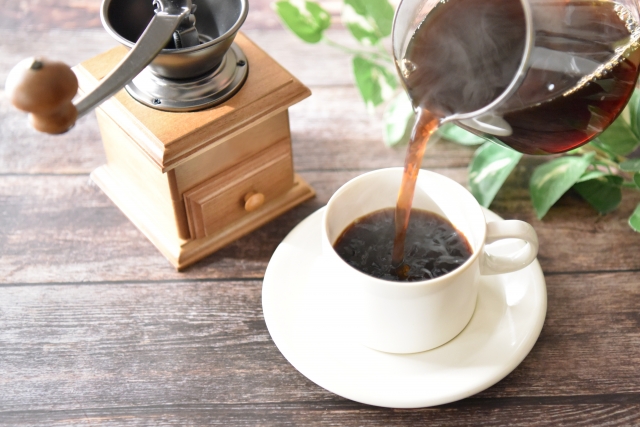 A cup of hot coffee being poured with a coffee bean grinder next to the cup
