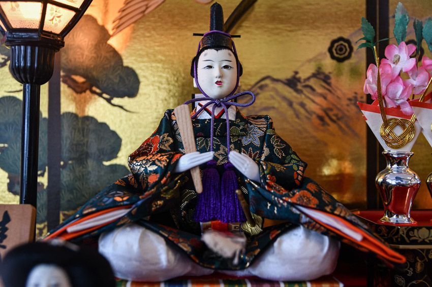 Japanese doll sitting on a cushion with a traditional gold panel backdrop