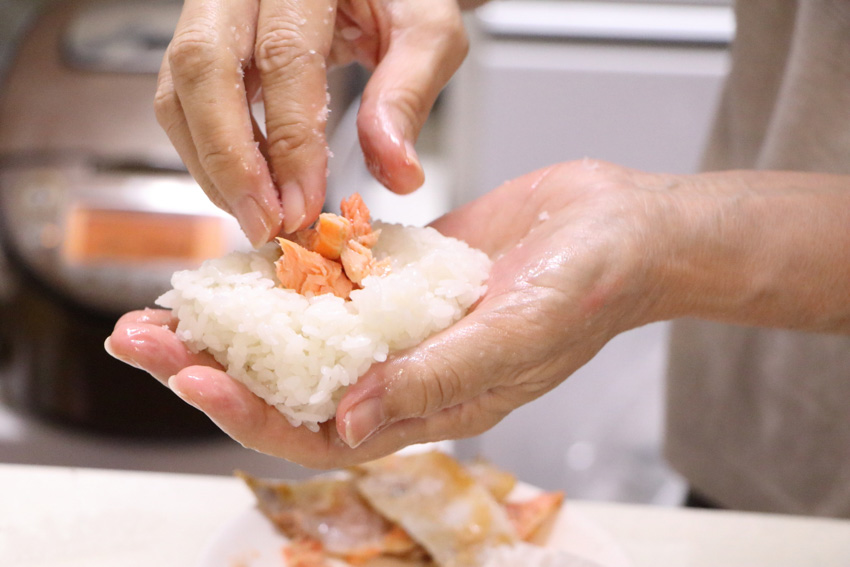 A person putting pieces of grilled salmon on top of a patty of rice.