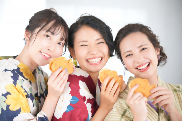 Three females wearing tradition japanese clothing and holding sweets on their hands