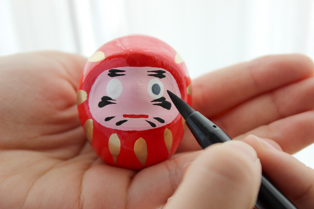 Close up of a tiny daruma being painted by a person