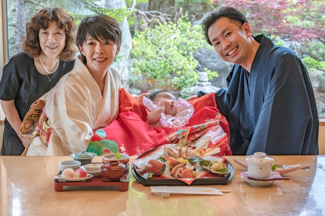 A couple holding their baby in front of the baby's first symbolic meal, a common tradition in Japan