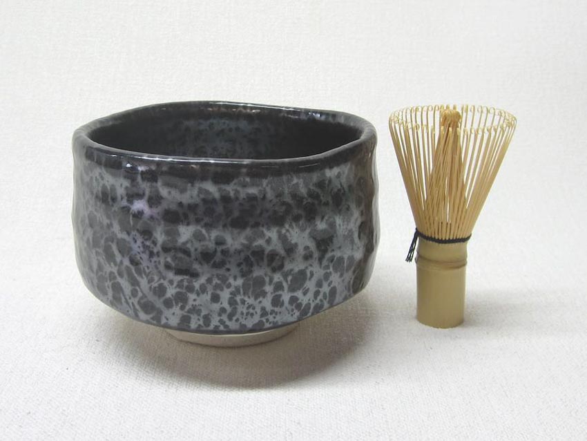 A greay and black matcha bowl with a bamboo whisk on the side