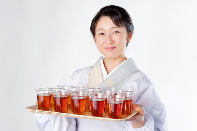 A female wearing a traditional kimono holding with her hand a tray full of tea cups