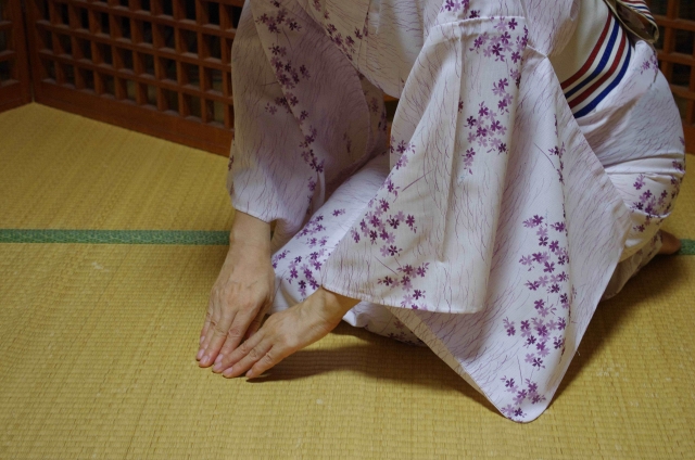 A person sitting on a tatami, wearing a traditional kimono with their hands touching the tatami floor 