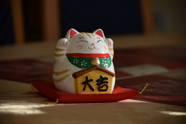 A maneki neko with closed eyes, both paws up and with a sign saying big luck in Japanese.