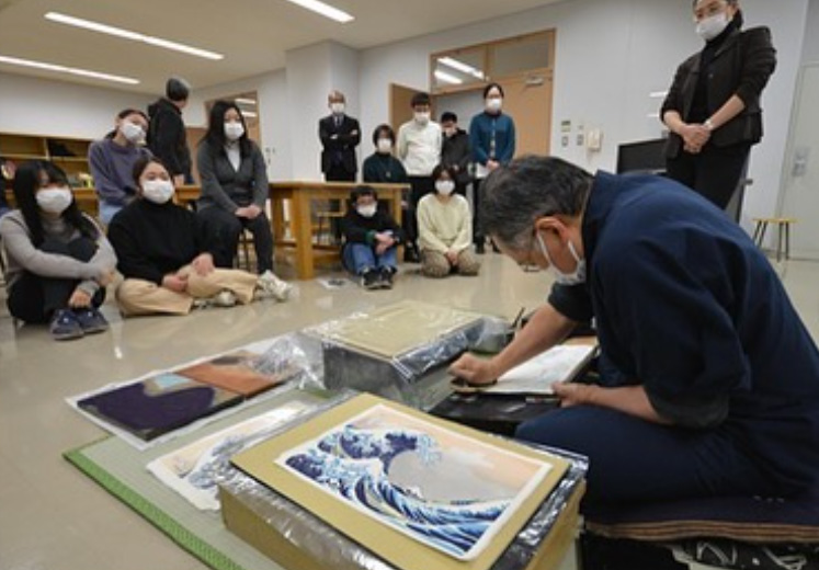 Man sitting on the floor printing The Great Wave Off Kanagawa in front of a group of people