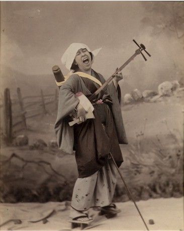 A person standing up playing the Shamisen