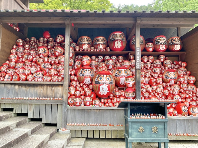 Hundreds of darumas in different sizes in a shed by a walk path