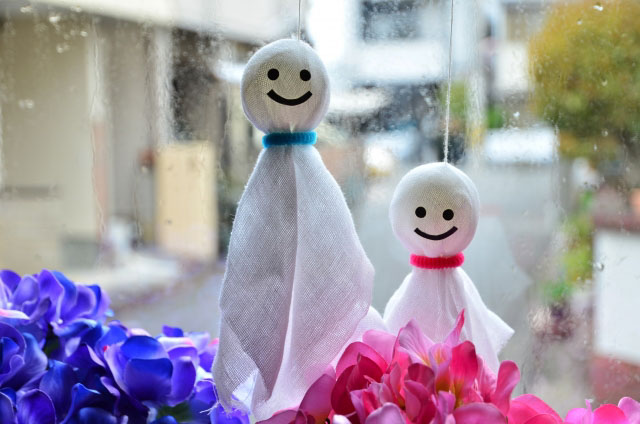 Two Teru Teru Bozu, one taller and one shorter hanging above pink and blue flowers