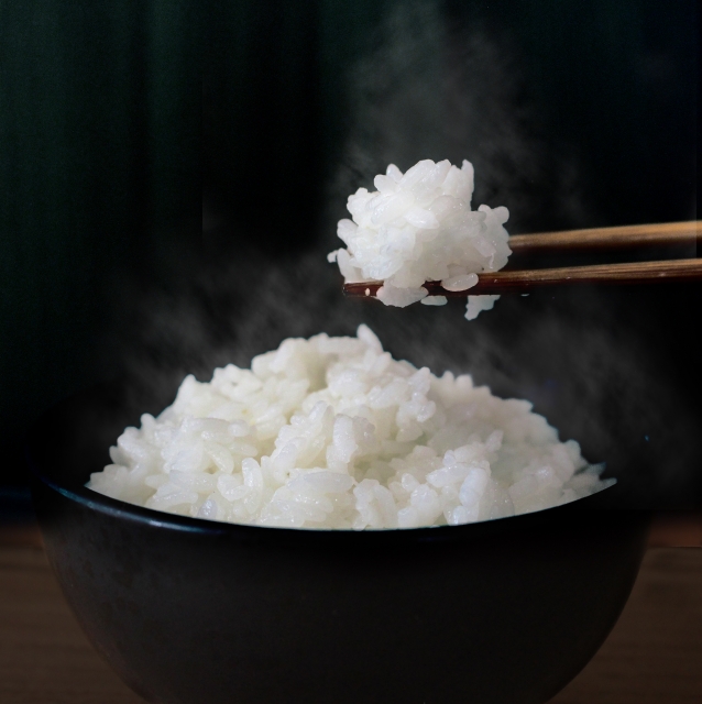 Close up image of someone picking up cooked white rice with chopsticks