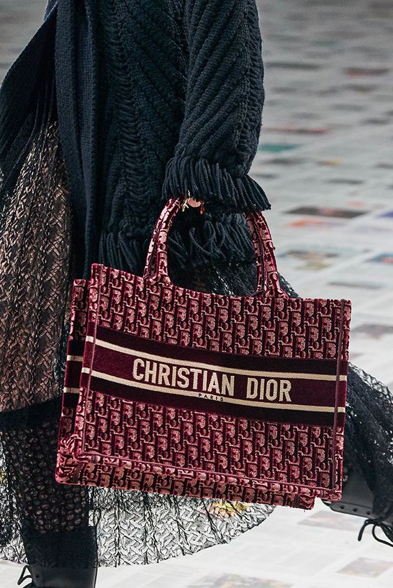 A model carrying a burgundy oblique Dior Book Tote bag 