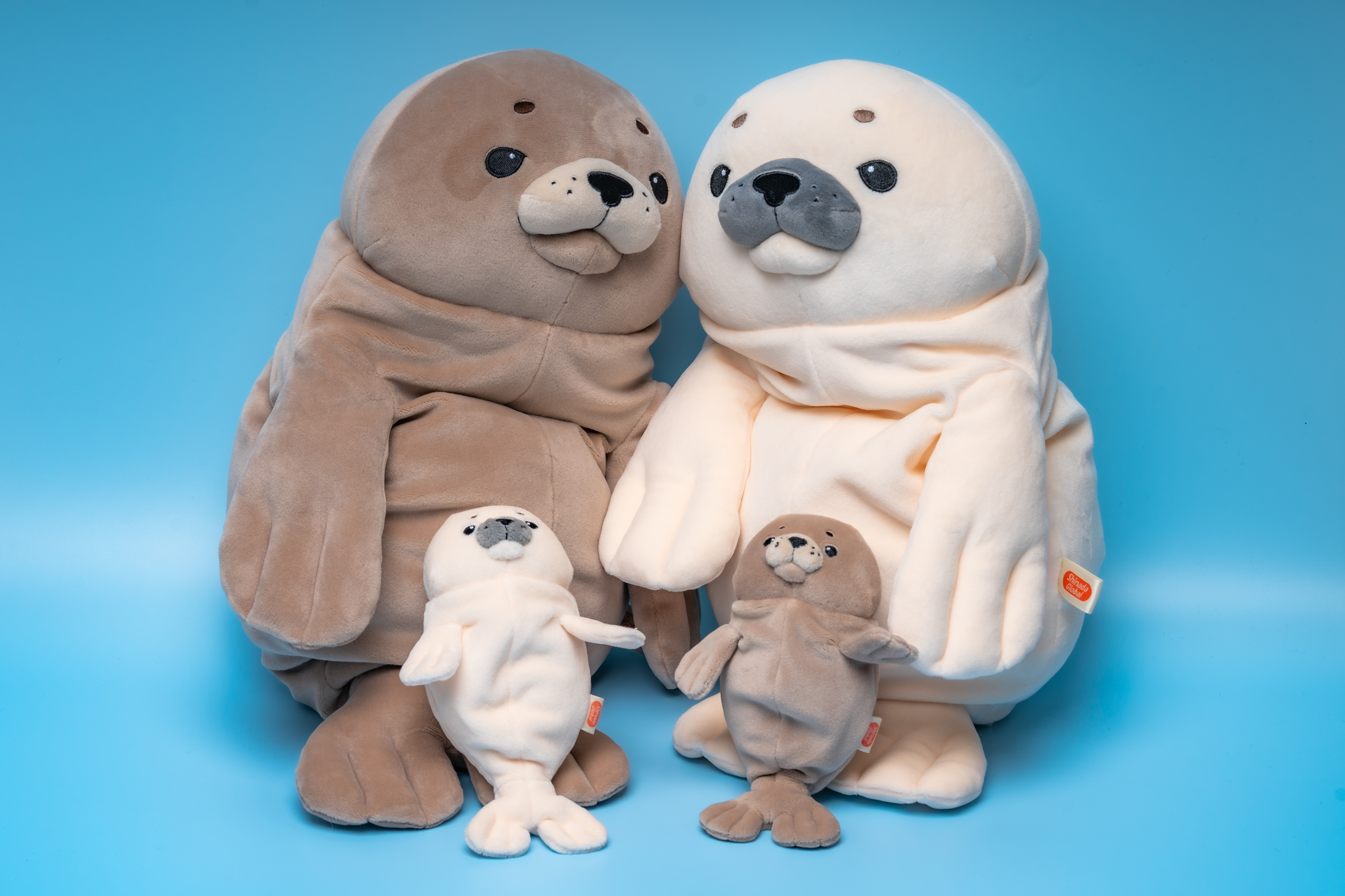 Gray and white large stuffed seal next to one another with mini gray and white seal leaning on them 