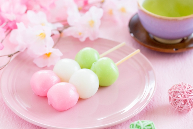 Two sticks with three dango on a pink plate with cherry flowers and Japanese tea.